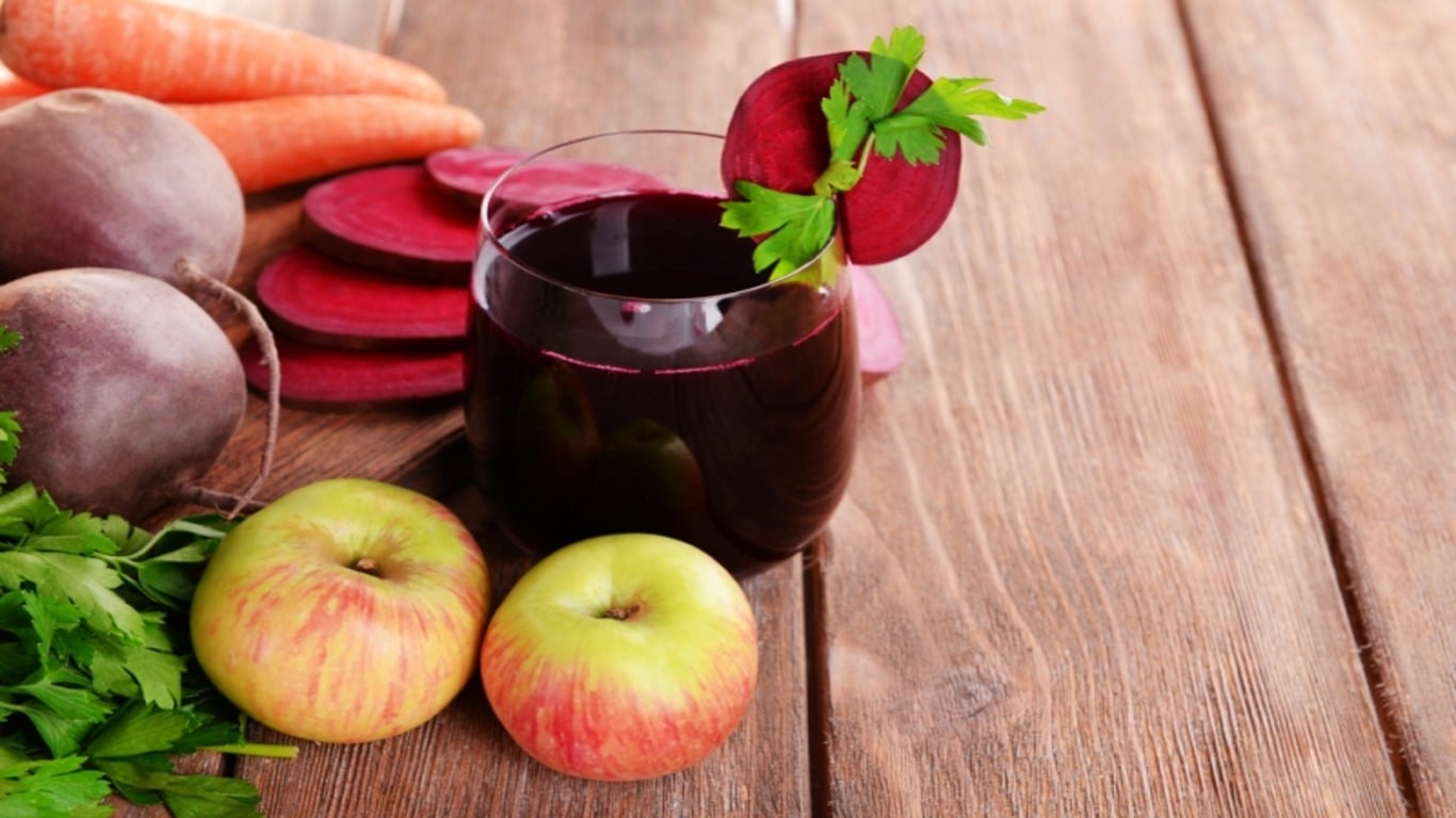 Glass of fresh beet juice and vegetables on wooden background